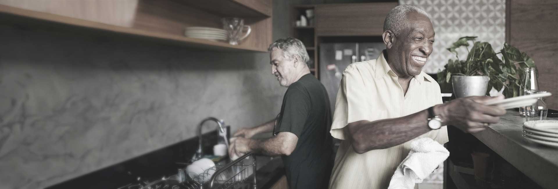 Two senior men washing dishes and smiling in a kitchen