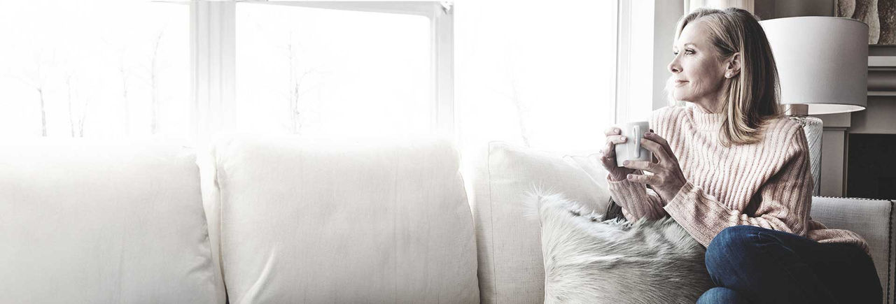 Woman sitting on sofa with coffee, looking out window