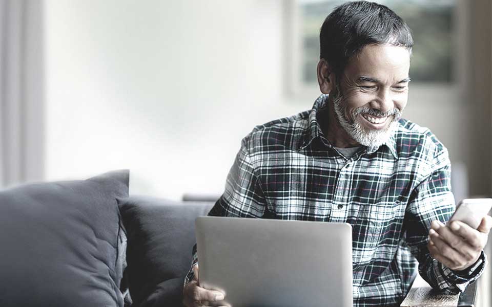 Man smiling while using laptop and smartphone at home