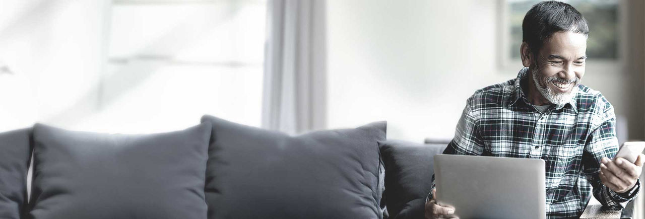 Man smiling while using laptop and smartphone at home