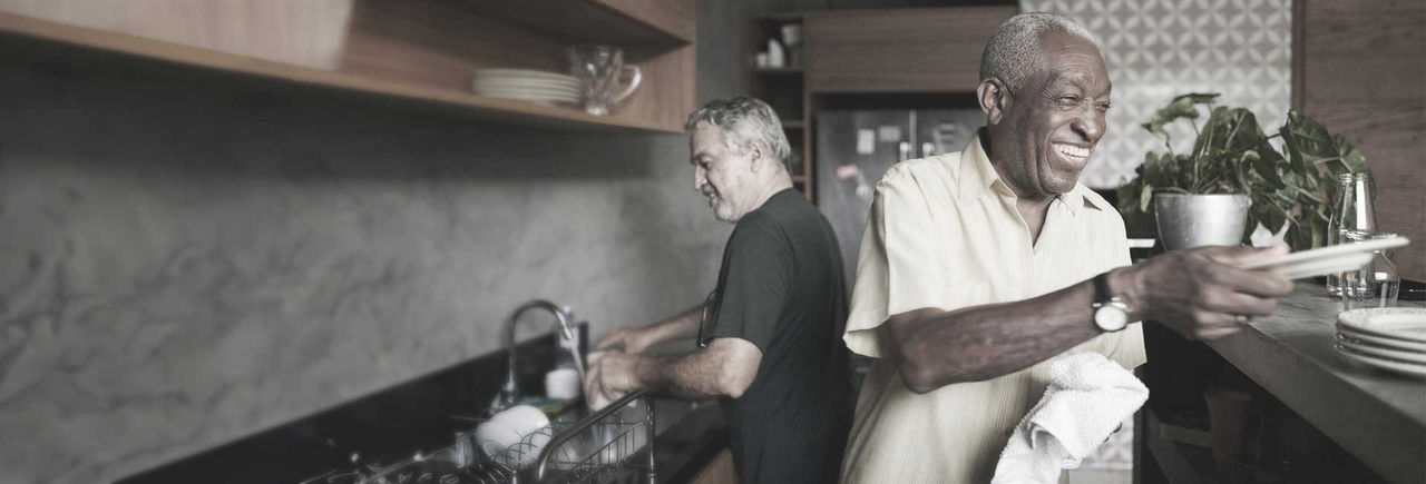Two senior men washing dishes and smiling in a kitchen